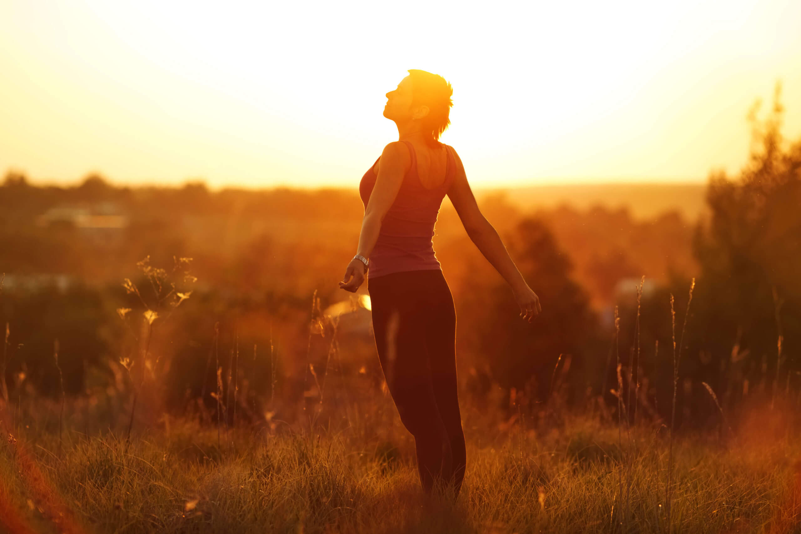 Fit happy woman in a field at sunset
