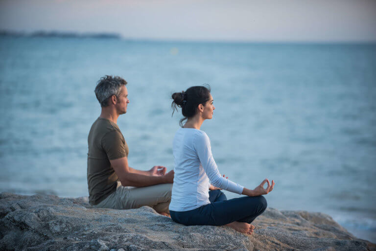 Couple practicing yoga at sunrise on the beach facing the sea